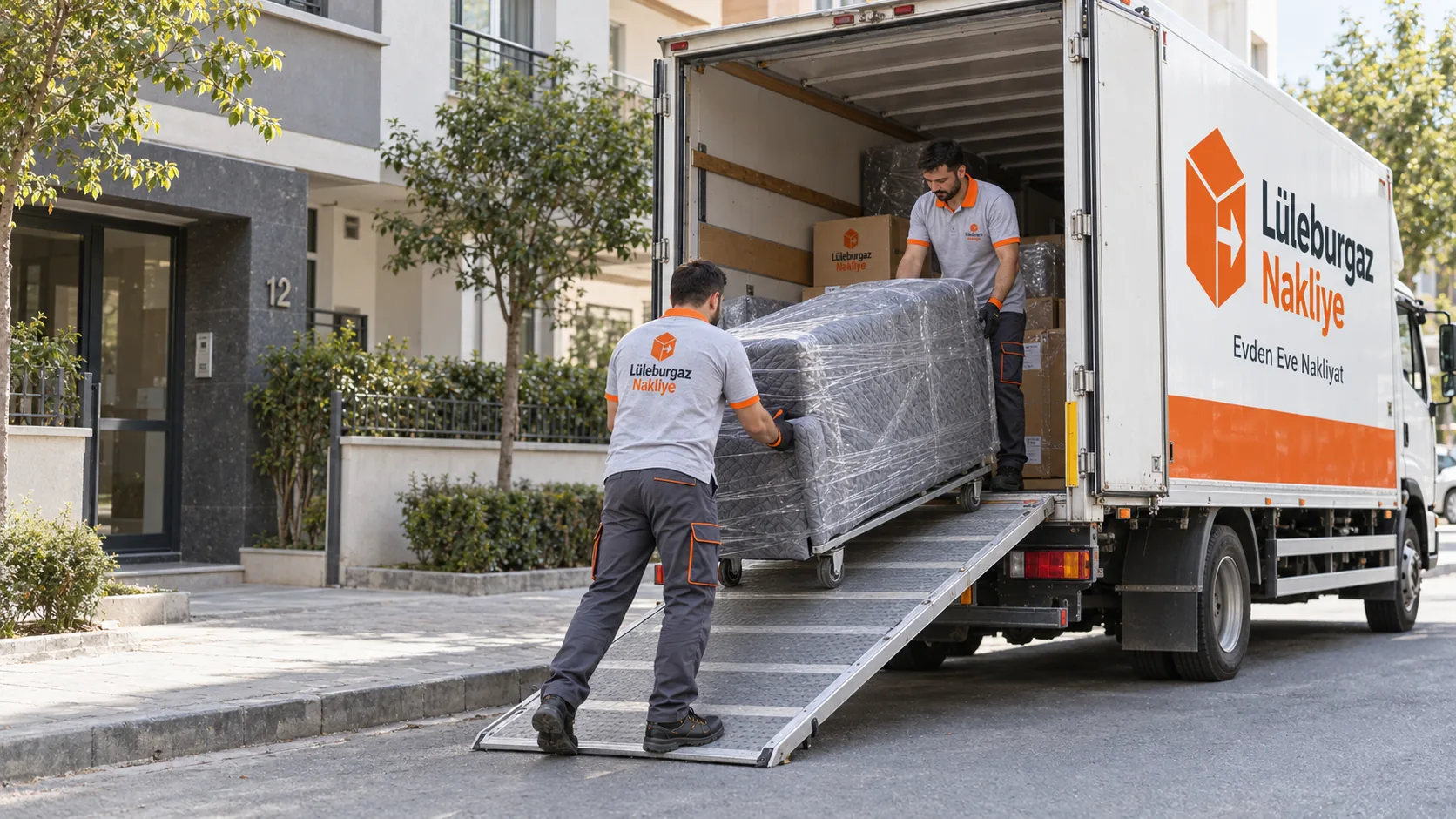 Apartman önünde sarılı koltuğu rampadan kamyona yükleyen iki nakliye görevlisi