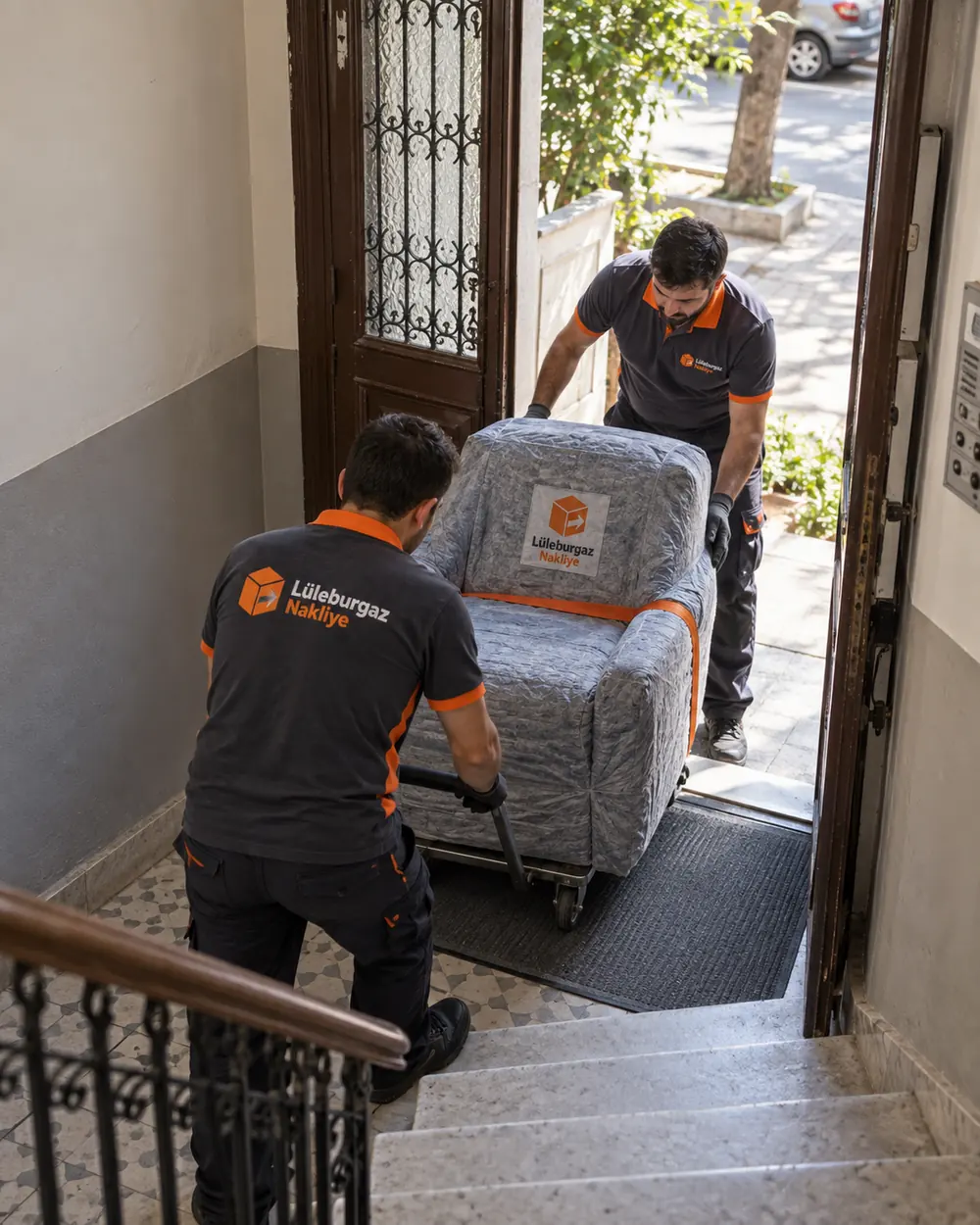 Eski apartman merdiveninde sarılı koltuğu birlikte taşıyan iki görevli